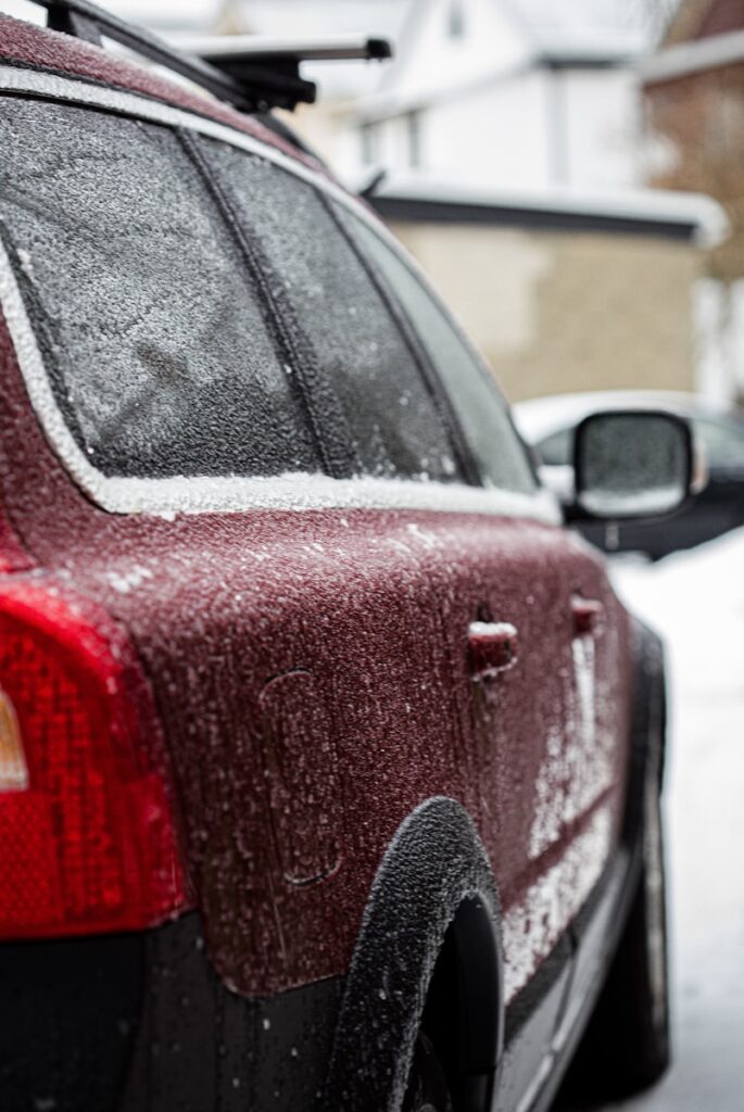 a red car parked on the side of the road covered in snow