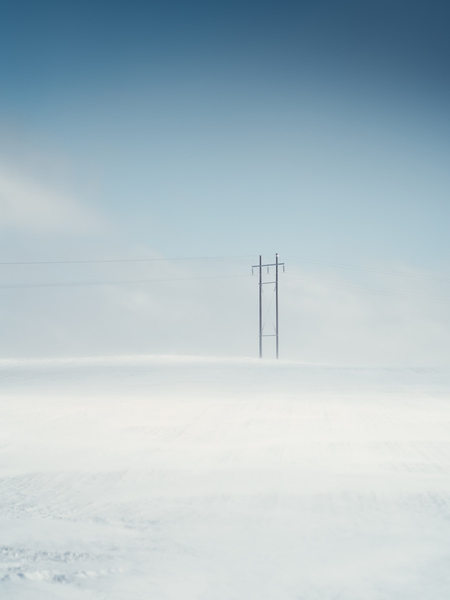 black electric post on snow covered ground under blue sky during daytime